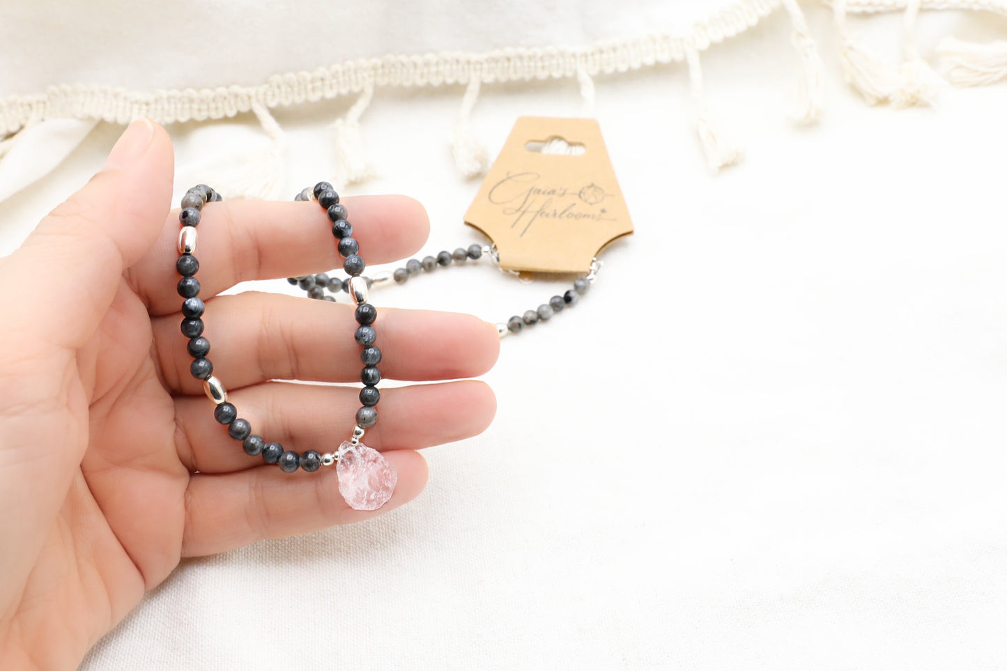 Female hand holding a Deep Grey Labradorite and Clear Quartz Necklace in 925 Sterling Silver.