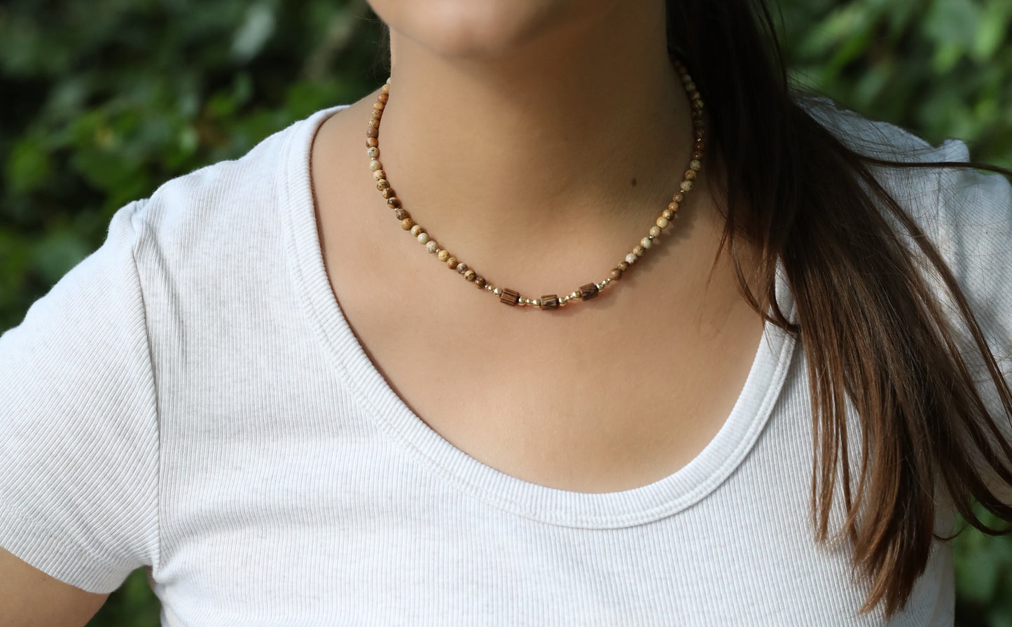 A model wearing The Earth's Story Necklace by Gaia's Heirlooms, made with Picture Jasper beads, natural wood and Gold Filled details.
