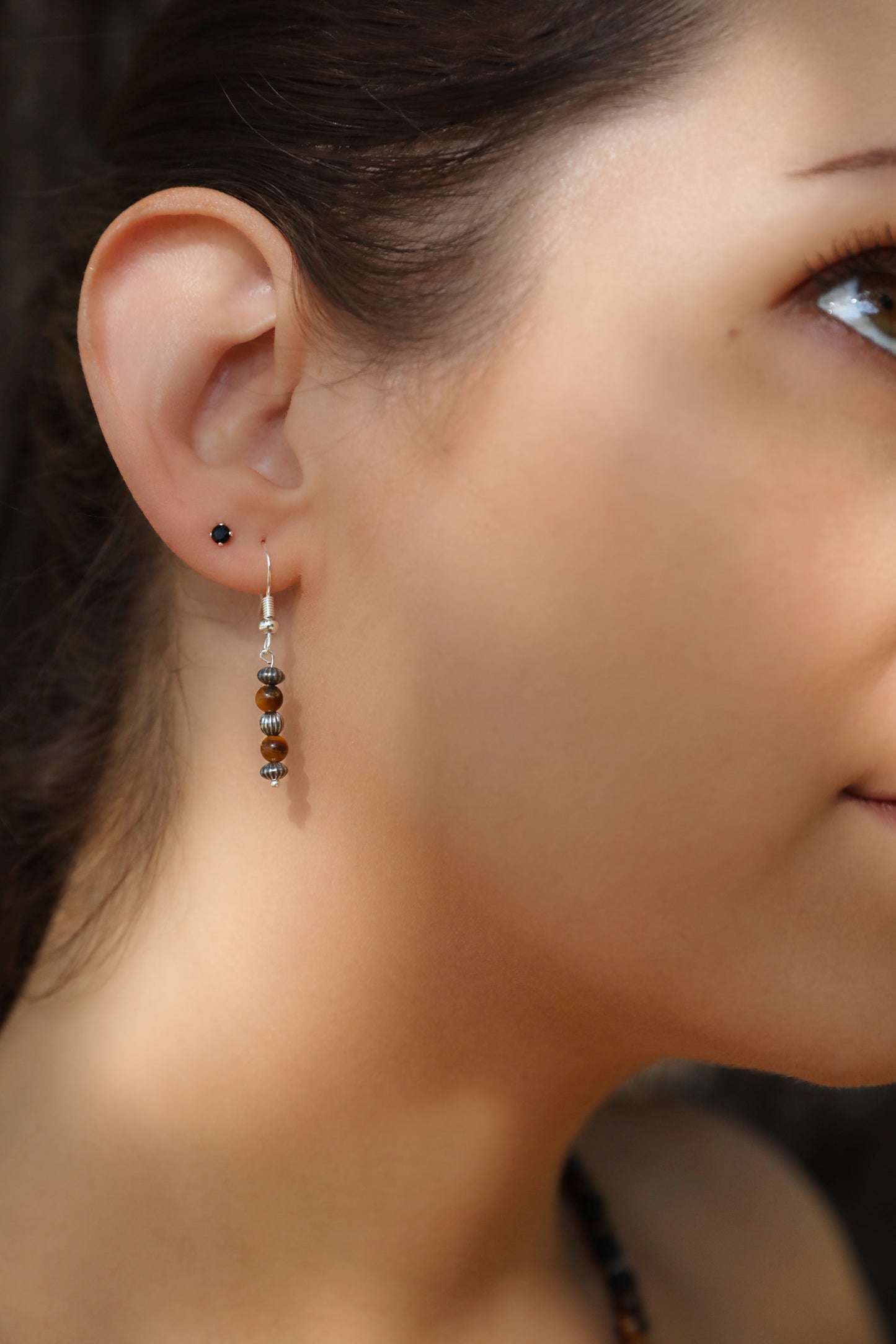 A model wearing The Fierce Wisdom Earrings from Gaia's Heirlooms, made with Tiger's Eye and oxidised Sterling Silver beads.
