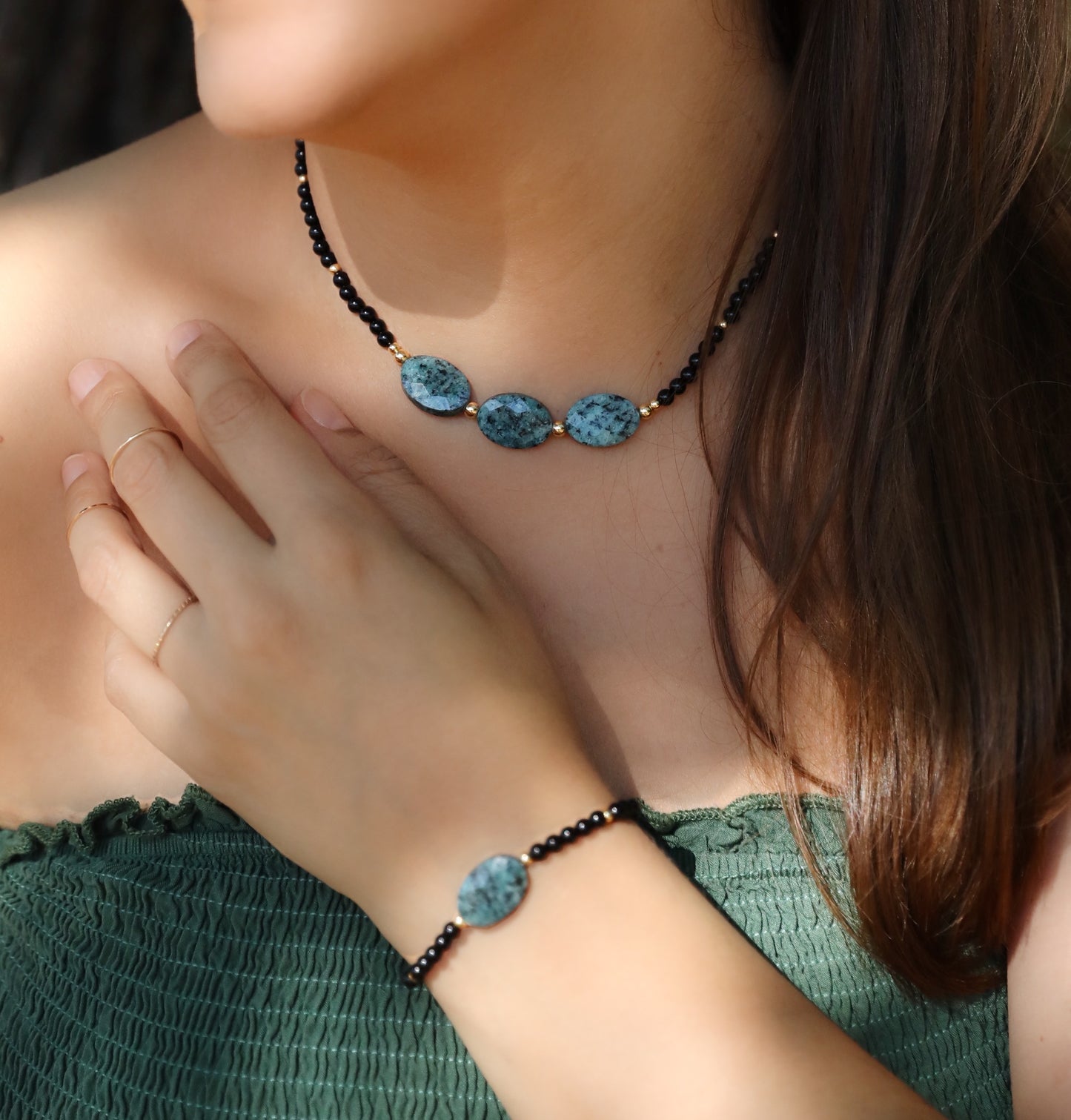 A model wearing The Fortifying Foundations Necklace and Bracelet by Gaiai's Heirlooms, made with Black Onyx beads, Blue Spot Jasper stones in the middle and Gold Filled details.
